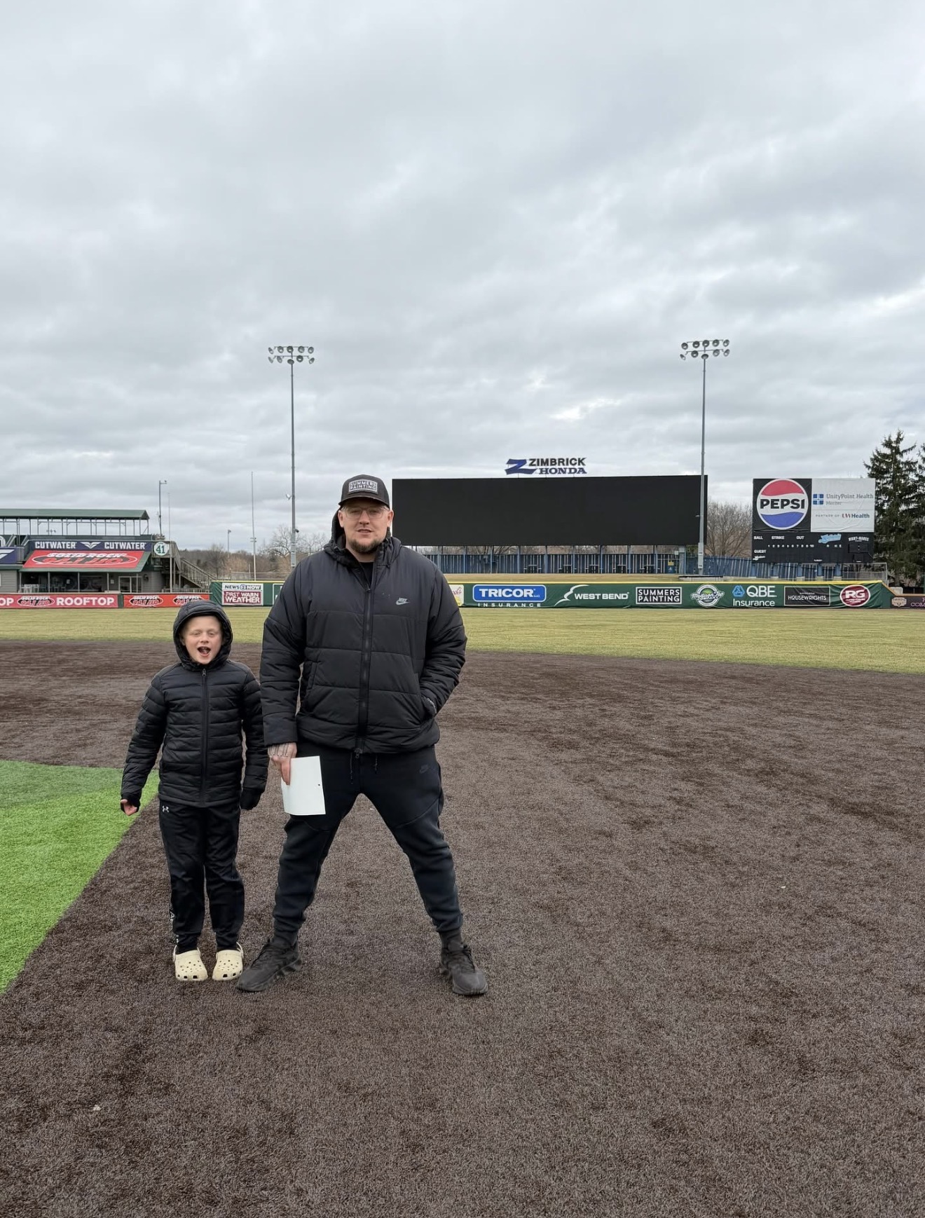 Scott Summers with son on the field near the Summers Painting banner